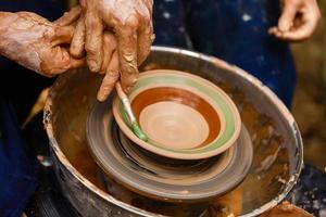 A potters hands guiding a child hands to help him to work with the ceramic wheel photo