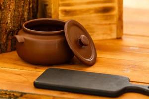 olla de cerámica sucia en la vieja tabla de cocina de madera