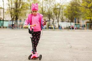 Little girl in a skirt sitting on a park bench listening to music and looking at mobile phone photo