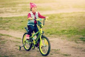 Child riding bike. Kid on bicycle in sunny park. Little girl enjoying bike ride on her way to school on warm summer day. Preschooler learning to balance on bicycle . Sport for kids. photo