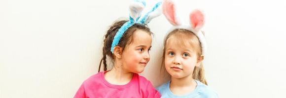 dos chicas sonrientes con orejas de conejo sosteniendo una caja con huevos de pascua en el fondo. foto
