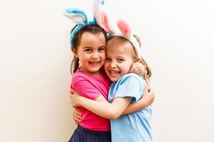 Two smiling girls with rabbit ears holding a box with easter eggs on background. photo