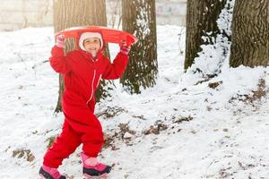 smiling little girl in her ski suit sliding down a small snow covered hill with her sledge photo