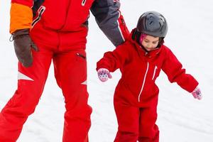 Little girl in red learning to ski with the help of an adult photo