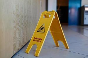 Low Section Of Worker Mopping Floor With Wet Floor Caution Sign On Floor photo