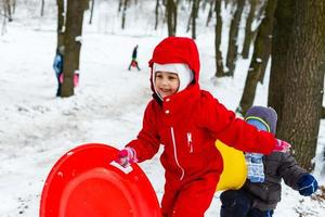 Pretty smiling little girl in her ski suit sliding down a small snow covered hill with her sledge photo