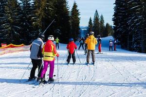 skier showing with ski poles on sun high in blue sky over winter mountains. Back view of resting during skiing on sunny winter day. Picturesque view of nature in mountains. Copy space. photo