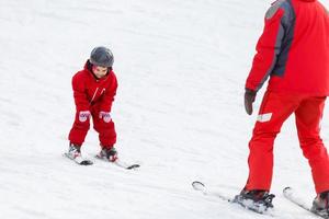 Professional ski instructor is teaching a child to ski on a sunny day on a mountain slope resort with sun and snow. Family and children active vacation. photo