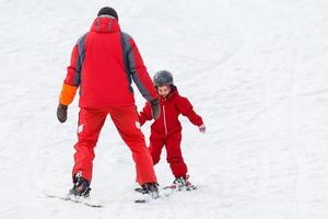 Professional ski instructor is teaching a child to ski on a sunny day on a mountain slope resort with sun and snow. Family and children active vacation. photo