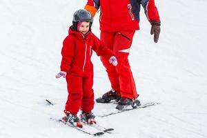 Little girl in red learning to ski with the help of an adult photo