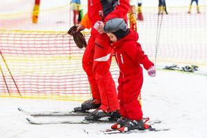 Little girl in red learning to ski with the help of an adult photo