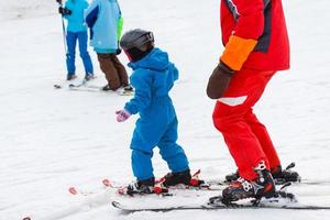 little girl learns to ski with the help of an adult photo