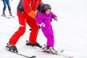 little girl learns to ski with the help of an adult photo