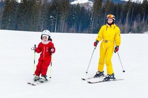 Little girl and a woman are skiing down a mountain photo