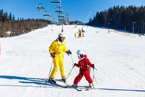 Mother and daughter having fun and learning skiing making first steps with mom's support on a ski winter resort at mountain hill. photo