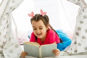 Portrait of pretty little girl reading book in cozy living room at home photo