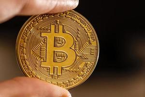Bitcoin gold coin in the hand of man on the background of the laptop on a white table