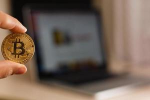 moneda de oro bitcoin en la mano del hombre en el fondo de la computadora portátil en una mesa blanca foto