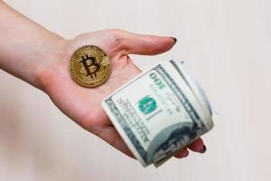 Golden bitcoin coin on women's hand on blurred us dollar bills background copy space photo