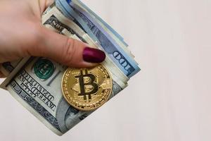 Golden bitcoin coin on women's hand on blurred us dollar bills background copy space photo