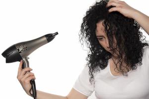 hermosa chica usando un secador de pelo y sonriendo. mujer joven natural secando el cabello rizado con máquina de secado de cabello. foto