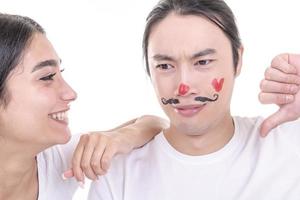 pareja mixta divirtiéndose. modelo femenino árabe dando beso a modelo masculino asiático que ha ahogado bigotes y corazón en su cara. aislado sobre fondo blanco. foto