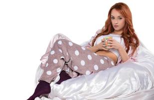 Young woman with cup of tea sitting on beanbag chair against white background photo