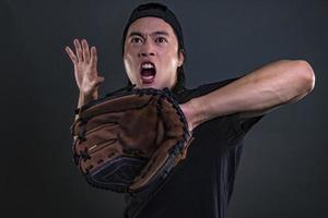 modelo masculino asiático con guante de béisbol aislado sobre fondo oscuro. concepto de jugador de béisbol foto