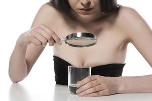 attractive woman looking in the glass of water with magnifying glass. isolated photo