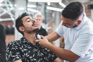 un apuesto hombre árabe está siendo afeitado por un peluquero en la barbería