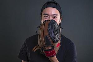 modelo masculino asiático con guante de béisbol aislado sobre fondo oscuro. concepto de jugador de béisbol foto