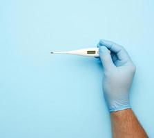 male hand in a blue medical glove holds a white plastic thermometer photo