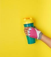 female hand holding plastic blue shaker bottle with a yellow cap photo