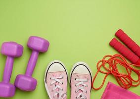 zapatillas de deporte, cuerda para saltar y dos mancuernas lilas sobre un fondo verde foto