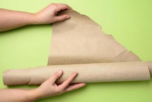 two female hands hold rolled brown paper, green background photo