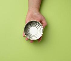 open metal round tin can in a female hand on a green background photo