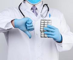 el médico terapeuta adulto está vestido con un abrigo uniforme blanco y guantes estériles azules está de pie y sosteniendo una pila de pastillas