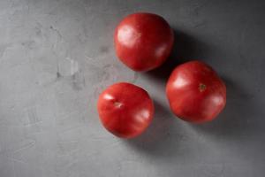 tres tomates rojos maduros sobre un fondo gris, vista superior foto