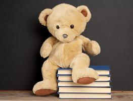 oso de peluche marrón sentado en una pila de libros, fondo negro foto