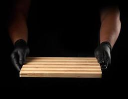 two male hands in black latex gloves hold an empty new brown wooden cutting board photo