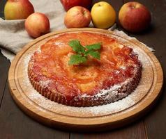 baked round apple pie on wooden board and fresh apples photo