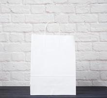 white paper bag with handles on white brick wall background, environmental material photo