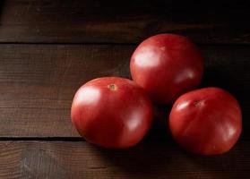 three ripe red tomatoes on a brown wooden background photo