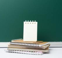 tablero escolar de tiza verde en blanco y pila de cuadernos, regreso a la escuela foto