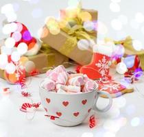 large ceramic cup with cocoa and marshmallows, behind a gift box and a Christmas garland photo