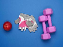 sports gloves, a pair of purple dumbbells and a red apple on a blue background, top view photo