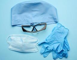 textile blue cap, disposable medical mask, pair of gloves and plastic glasses photo