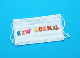 disposable medical face mask and lettering new normal on blue background photo