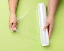 two female hands hold a roll of transparent cling film for packaging products photo