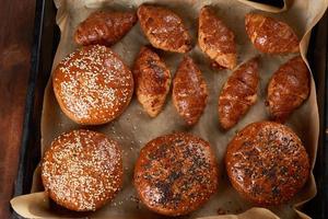 croissants horneados y bollos redondos con semillas de sésamo en una bandeja para hornear de hierro con papel para hornear marrón enrollado foto